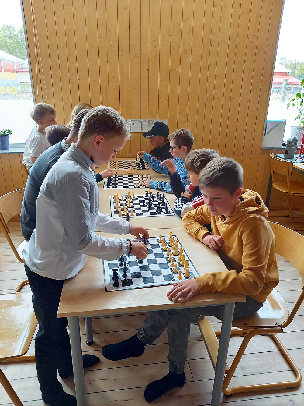 Ett bord med fyra schackbräden på rad med barn vid respektive bräde som spelar mot varandra.